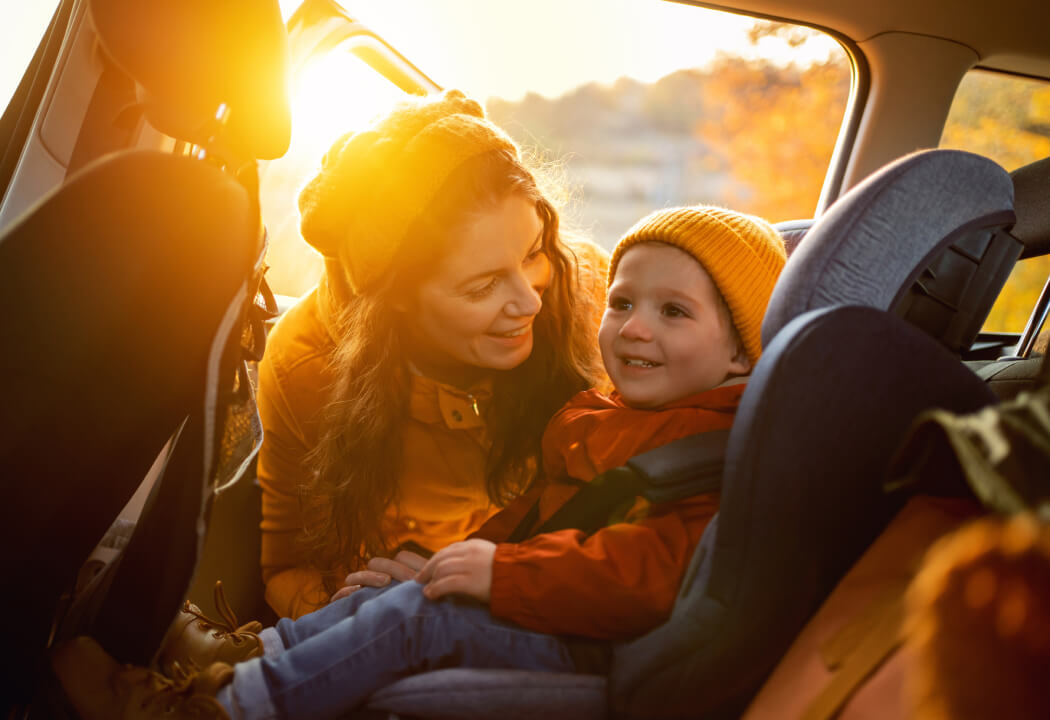 A mother buckling a young child into a car seat