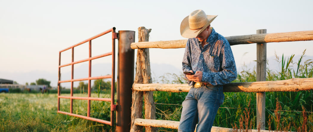 Cowboy leaning against a wooden fence looking at a smartphone 
