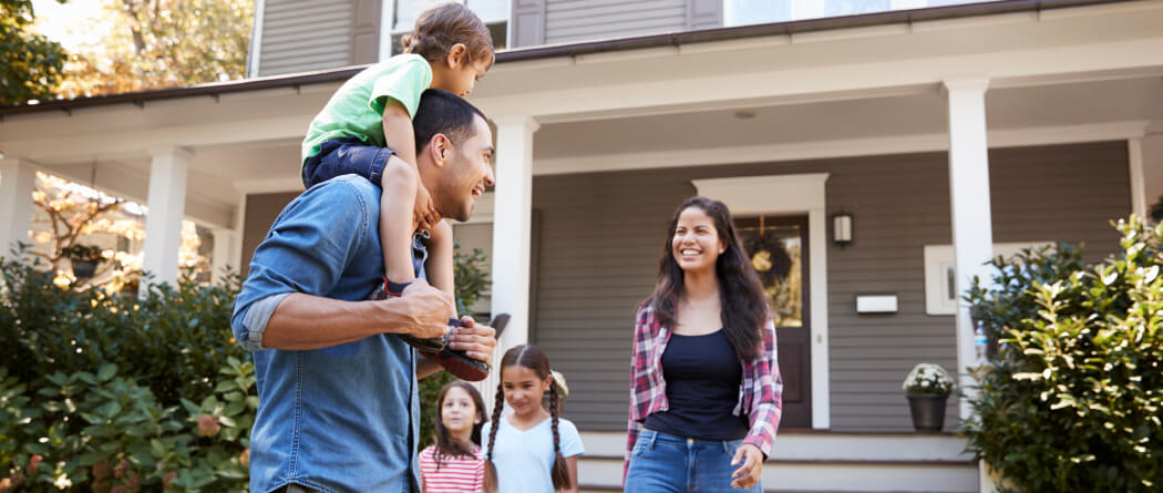 A young family standing outside a large house