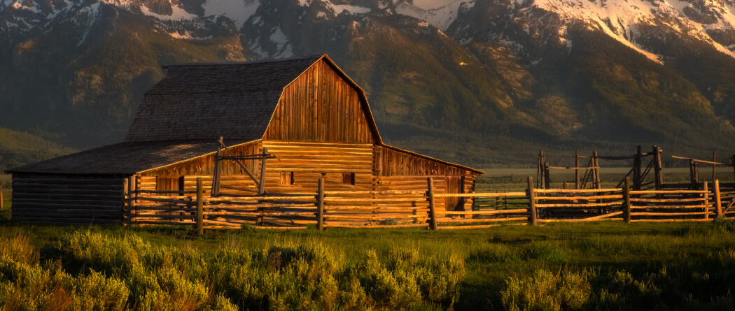 A large wooden barn with mountains in the background